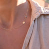 Woman with a 14k yellow gold Classic necklace featuring one white topaz and one 1/4” flat disc engraved with the letter H