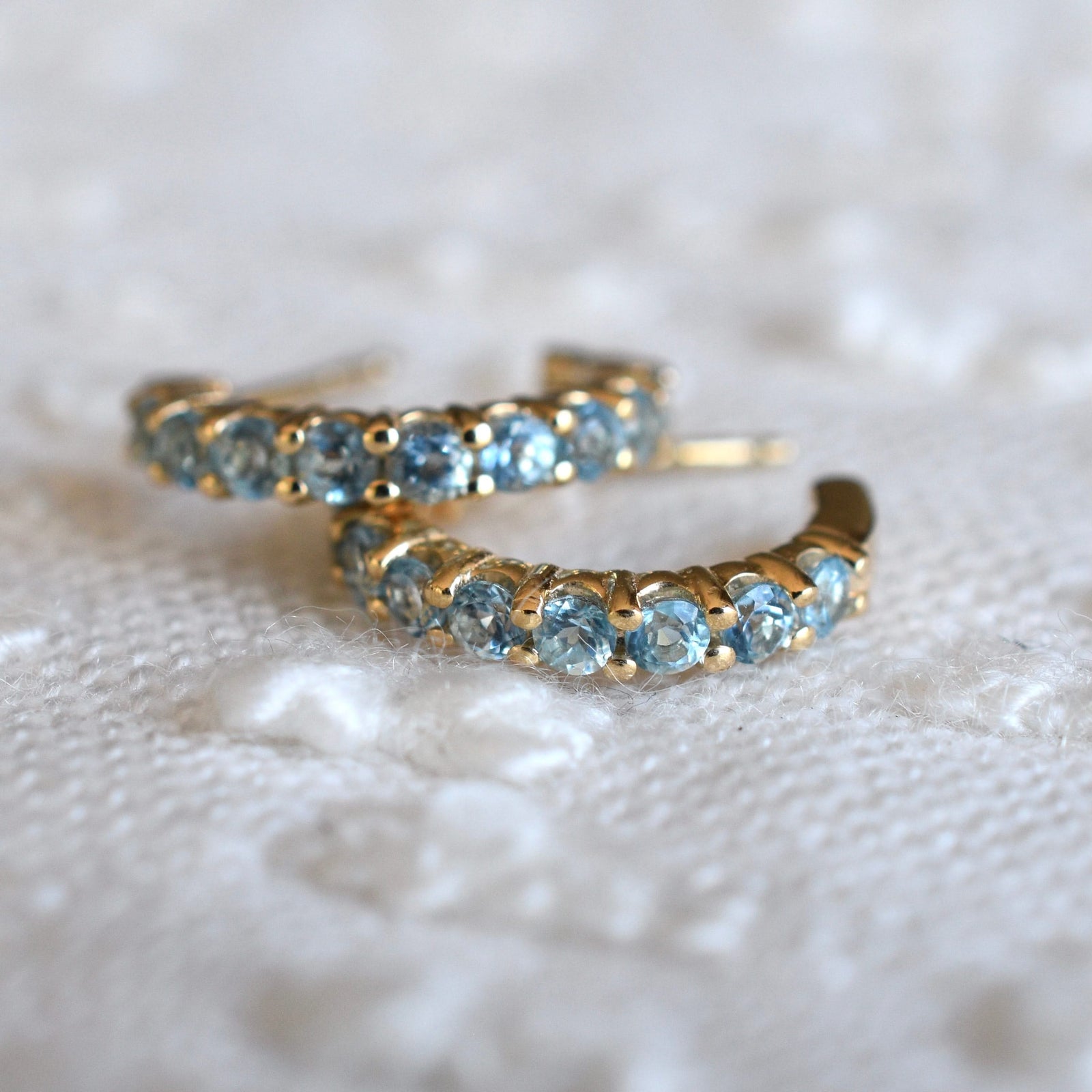 A pair of Rosecliff huggie earrings in 14k gold each featuring nine 2mm faceted round cut prong set Nantucket blue topaz