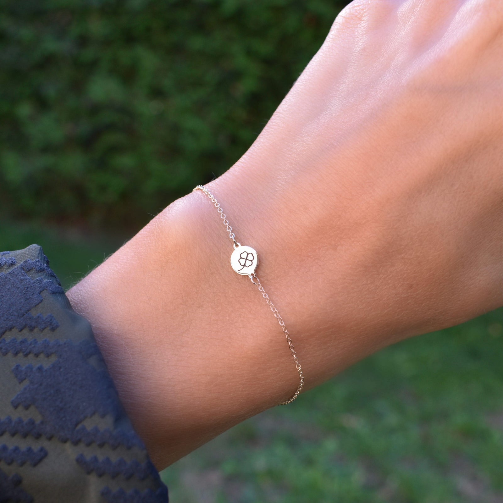 Woman wearing a 14k yellow gold Classic cable chain bracelet featuring one 1/4” flat disc engraved with a four leaf clover