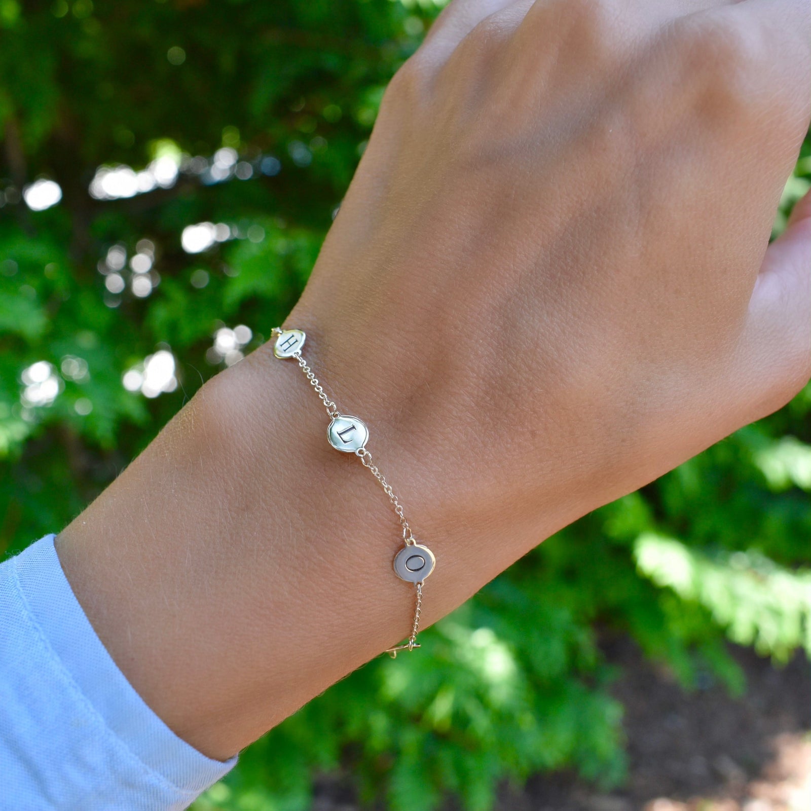 Woman wearing a 14k yellow gold cable chain bracelet featuring 1/4” flat discs engraved with letters