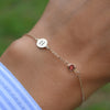 Woman wearing a 14k yellow gold Classic bracelet featuring one garnet and one 1/4” flat disc engraved with the letter H
