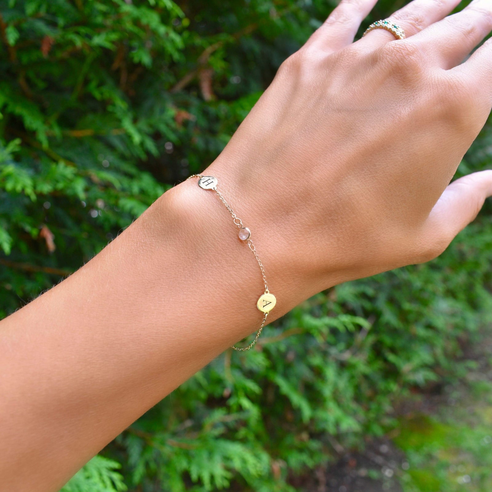 Woman wearing a 14k yellow gold Classic bracelet featuring one birthstone and two 1/4” flat discs engraved with letters H & A