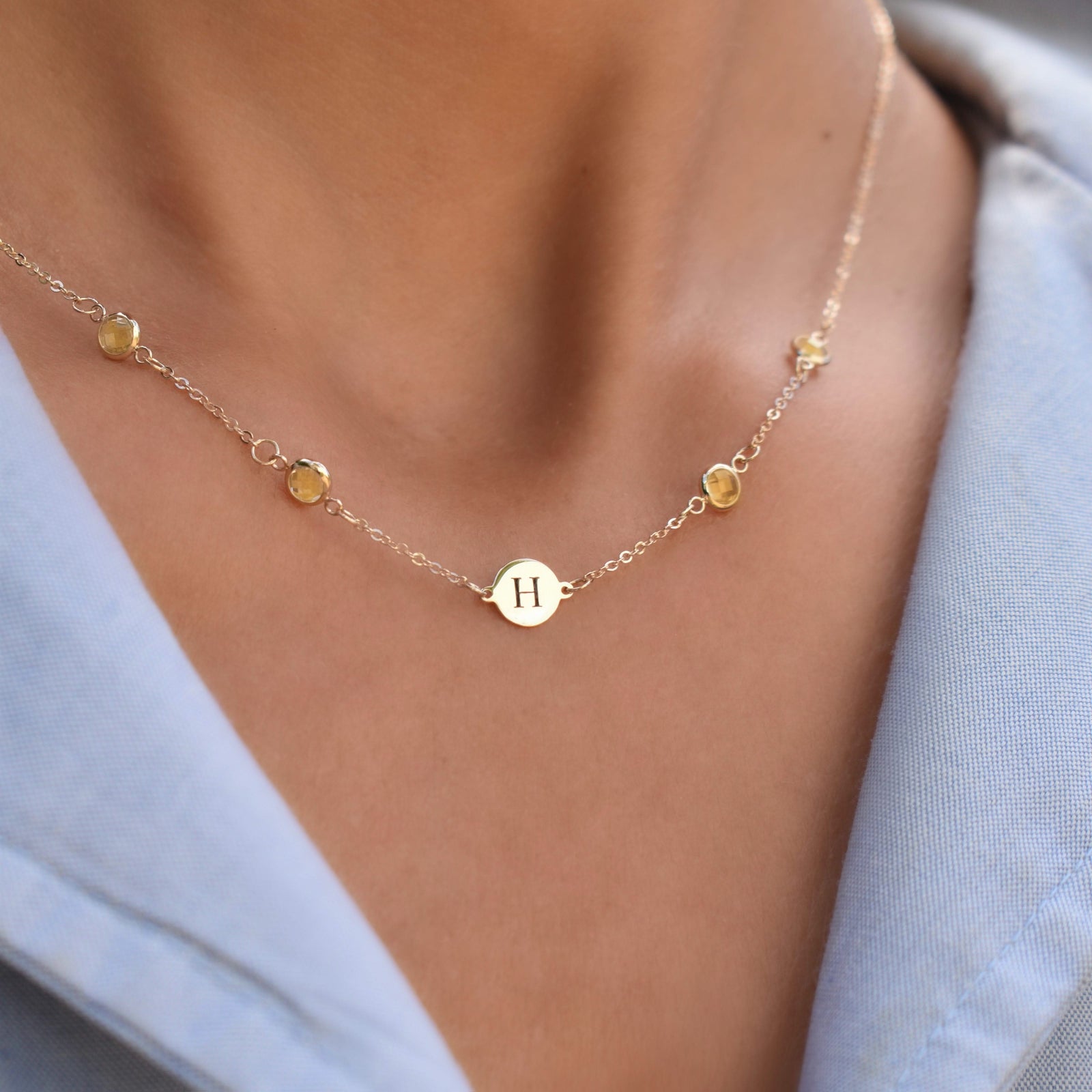 Woman with a 14k yellow gold Classic necklace featuring four citrines and one 1/4” flat disc engraved with the letter H