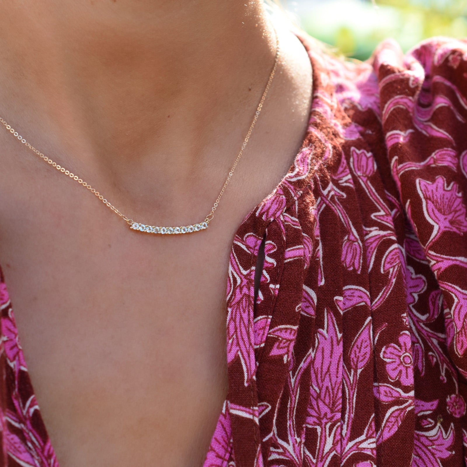 Woman wearing a Rosecliff bar necklace featuring eleven 2 mm faceted round cut aquamarines prong set in 14k yellow gold