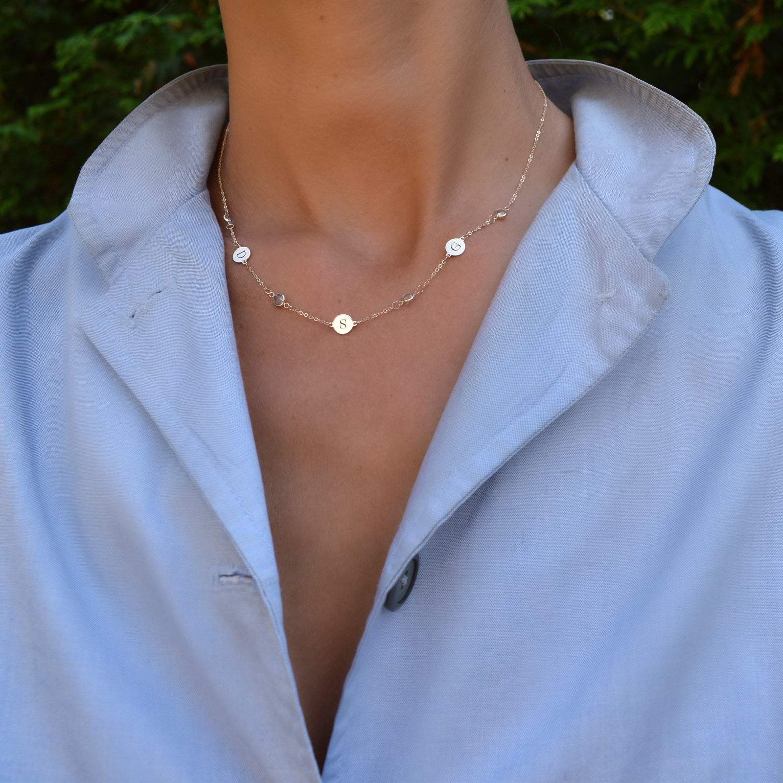 Woman wearing a 14k gold Classic necklace featuring 4 birthstones and three 1/4” flat letter-engraved discs
