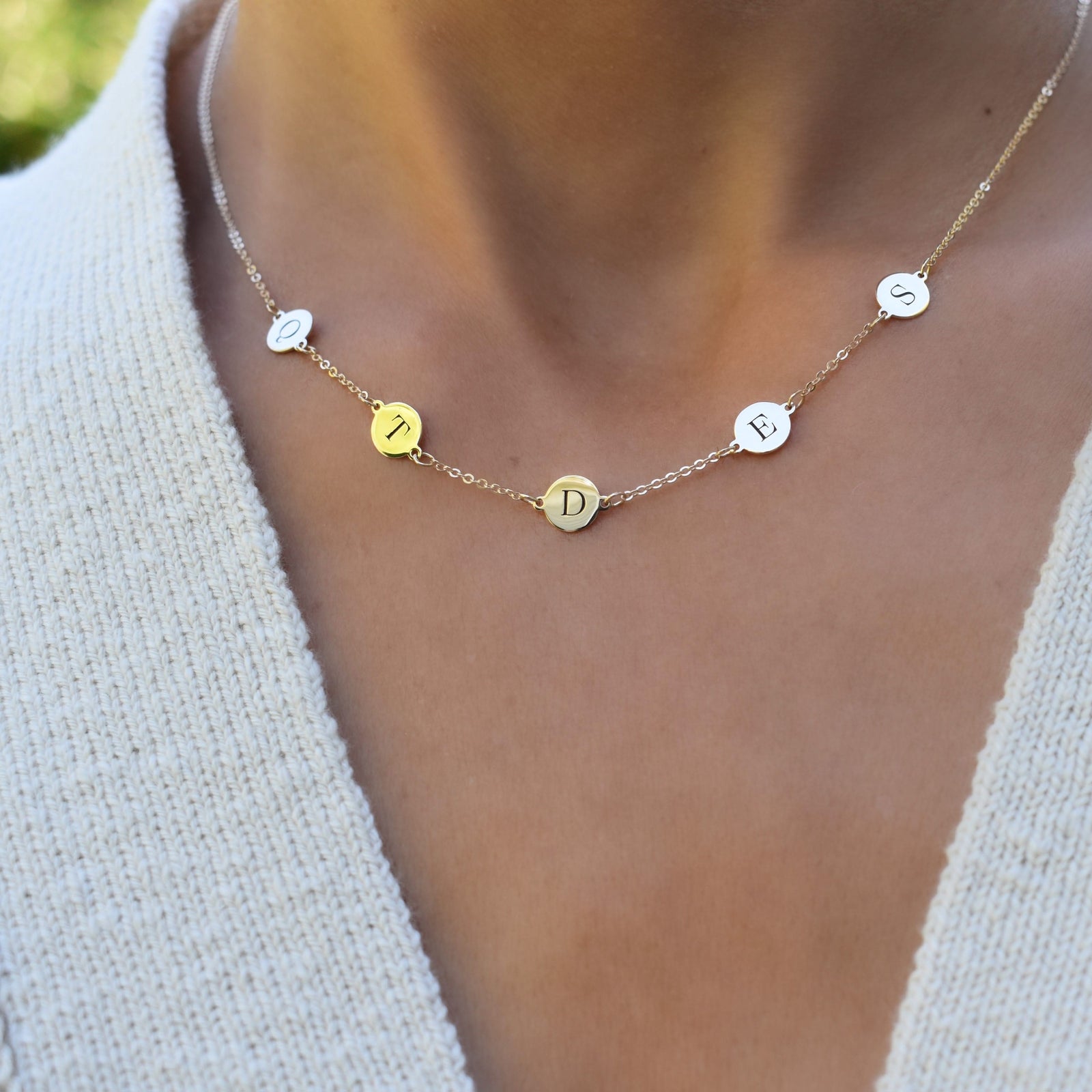 Woman with a 14k yellow gold cable chain necklace featuring five 1/4” flat letter-engraved discs