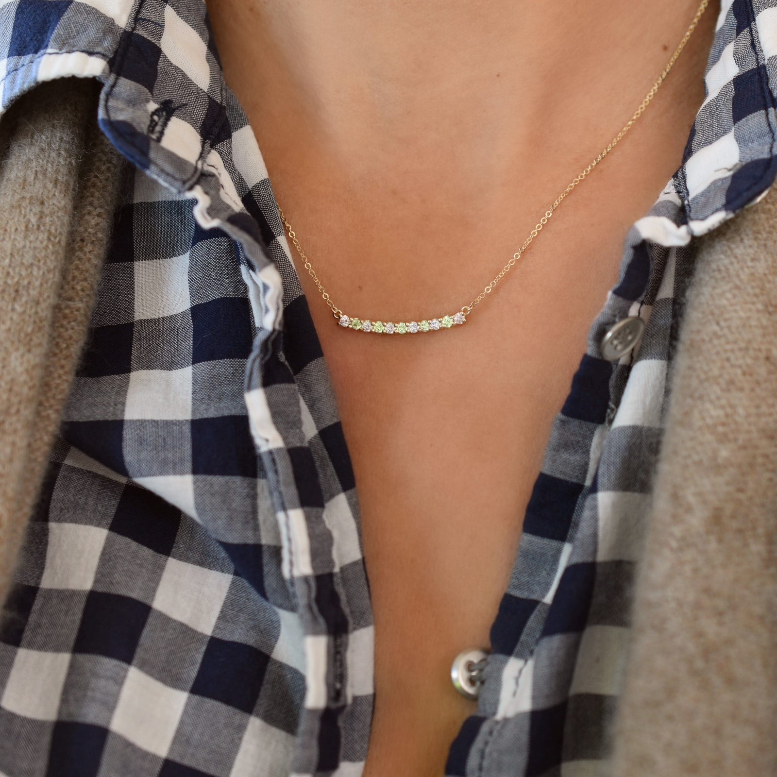 Woman wearing a Rosecliff bar necklace with eleven alternating 2 mm round cut peridots and diamonds prong set in 14k gold