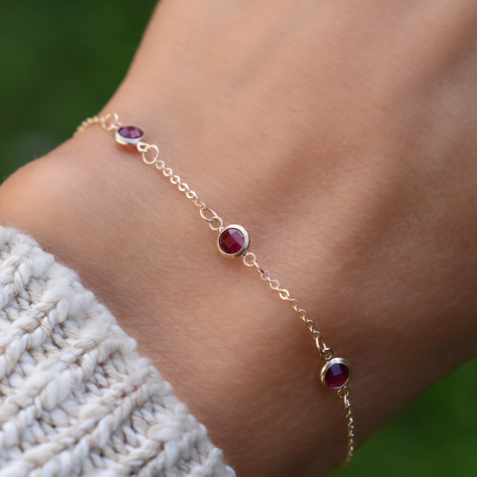 Woman with a Bayberry 1.17 mm cable chain birthstone bracelet featuring three 4 mm briolette rubies bezel set in 14k gold