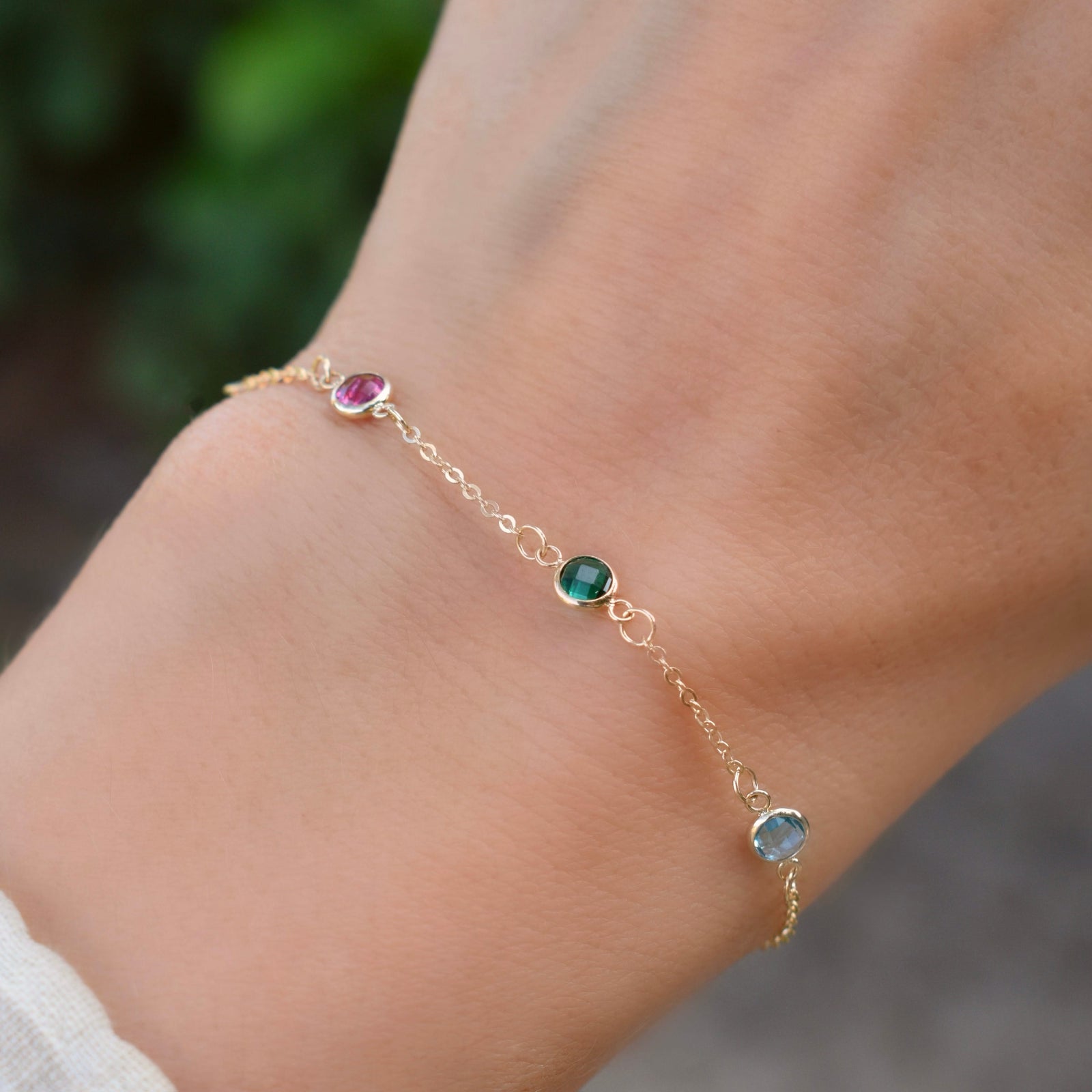 Woman with a Personalized cable chain bracelet featuring three 4 mm briolette cut gemstones bezel set in 14k yellow gold