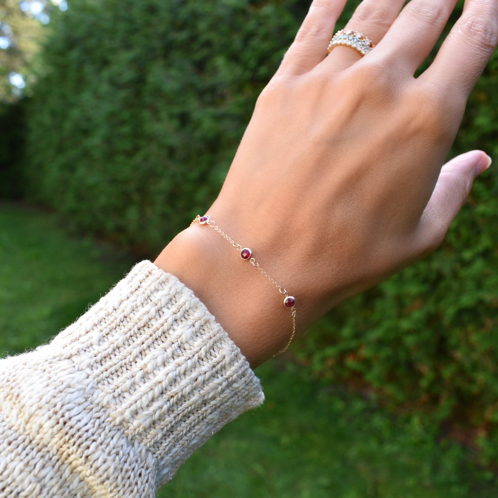 Woman wearing a Bayberry 1.17 mm cable chain birthstone bracelet featuring three 4 mm briolette rubies bezel set in 14k gold