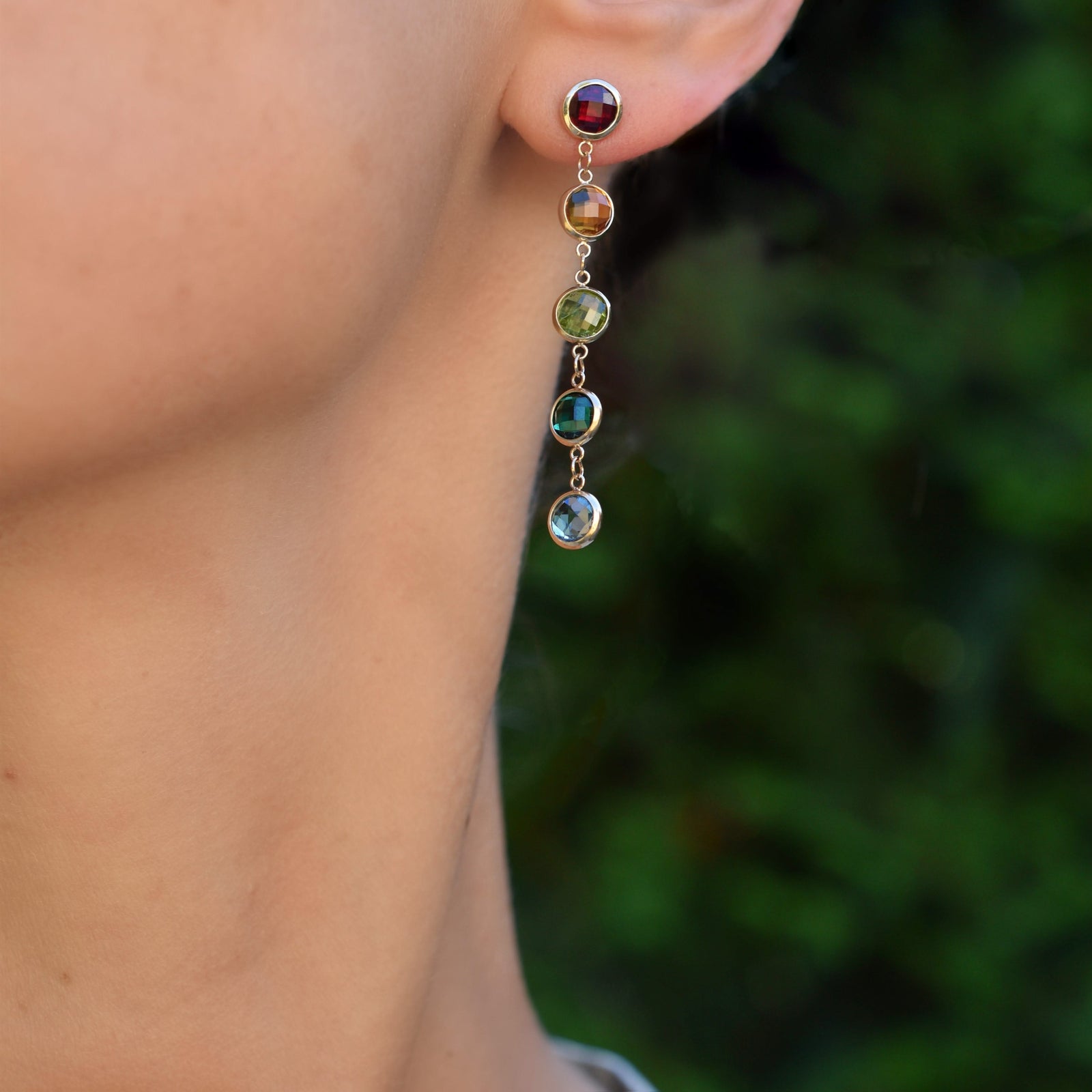 Woman wearing a 14k yellow gold Grand stud earring each featuring five 6 mm briolette cut rainbow hued gemstones