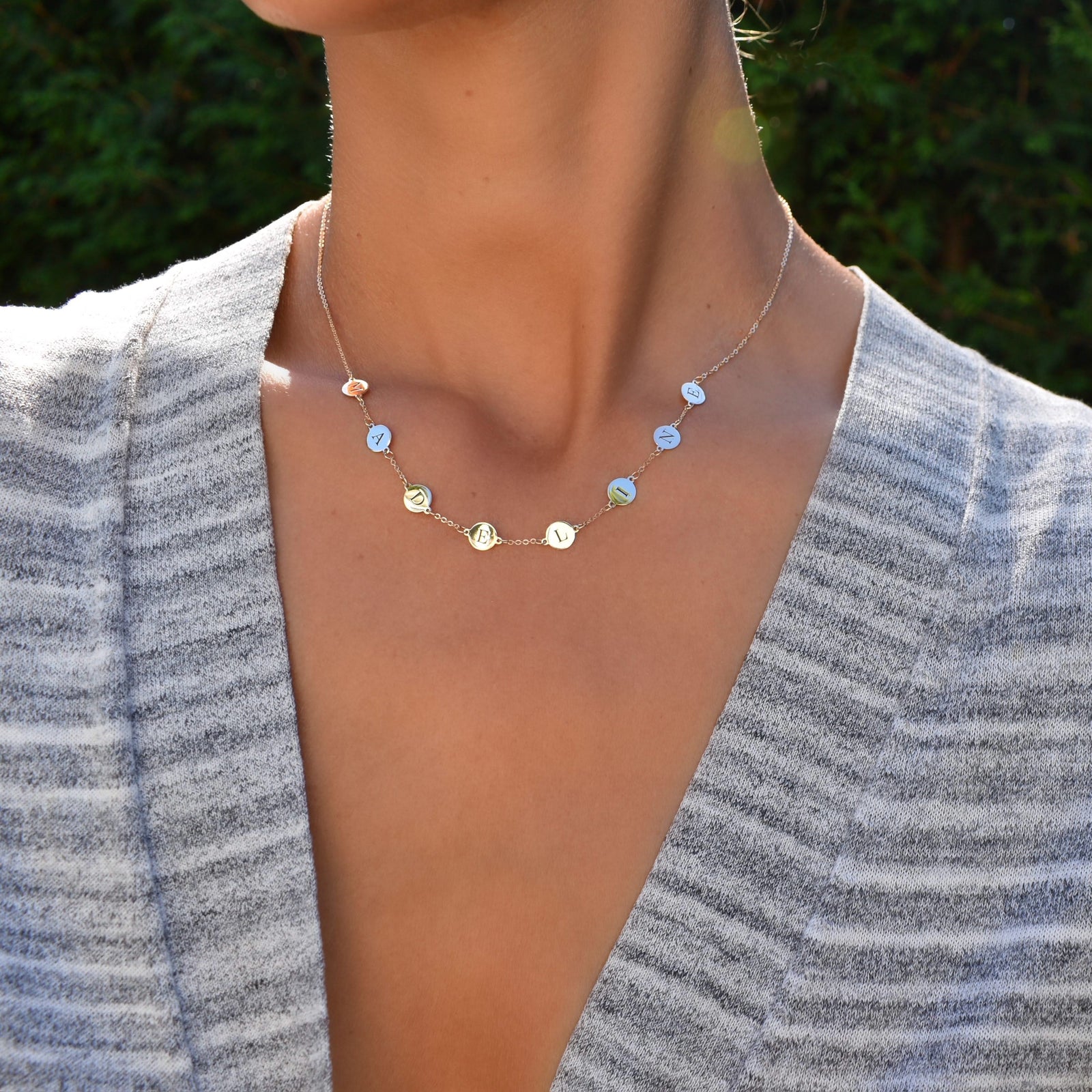 Woman wearing a 14k yellow gold cable chain necklace featuring eight 1/4” flat discs engraved with letters