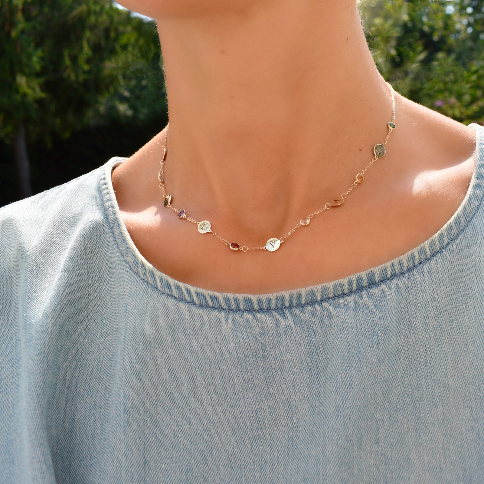Woman wearing a 14k yellow gold Classic necklace featuring six round birthstones and six 1/4” flat letter-engraved discs