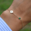 Woman's hand with a 14k yellow gold Classic bracelet featuring one emerald and one 1/4” flat disc engraved with the letter H