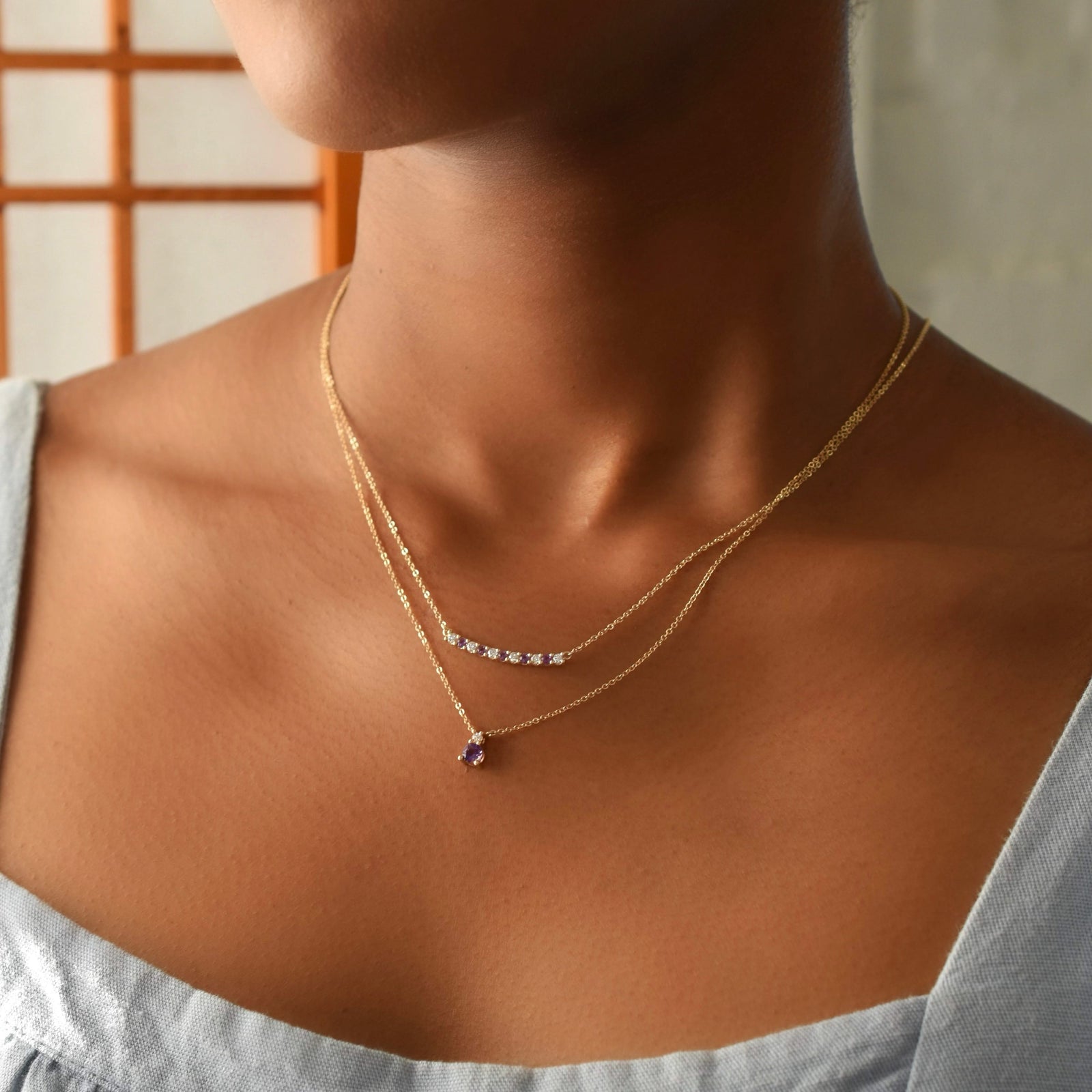Woman with two gold necklaces including a Rosecliff bar necklace with eleven alternating 2 mm faceted amethysts and diamonds