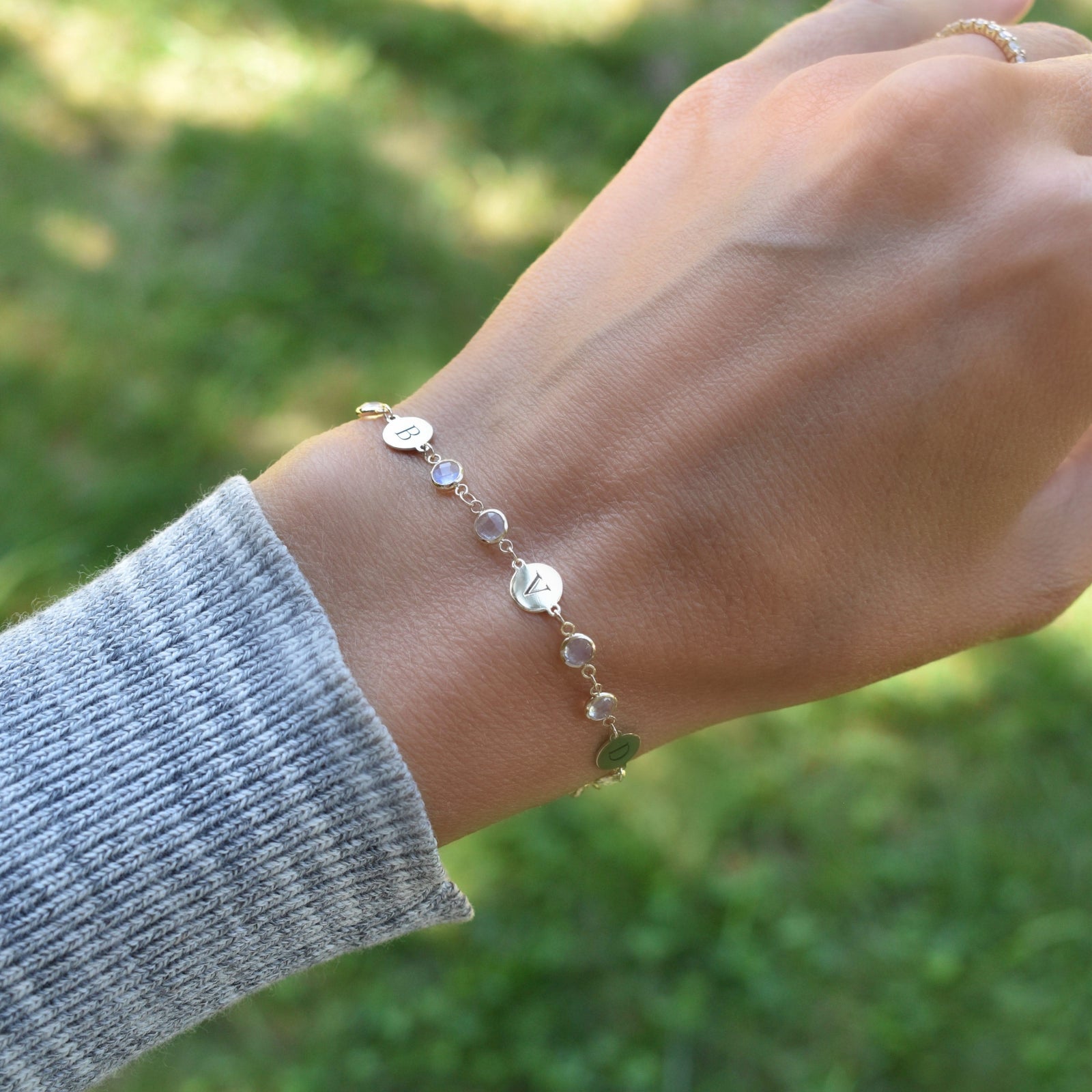 Woman with a Newport gold bracelet featuring 4 mm gemstones and 1/4” flat letter-engraved discs