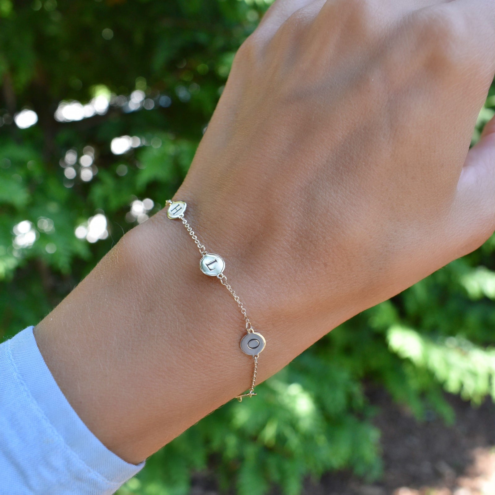 Woman wearing a 14k yellow gold cable chain bracelet featuring 1/4” flat discs engraved with letters