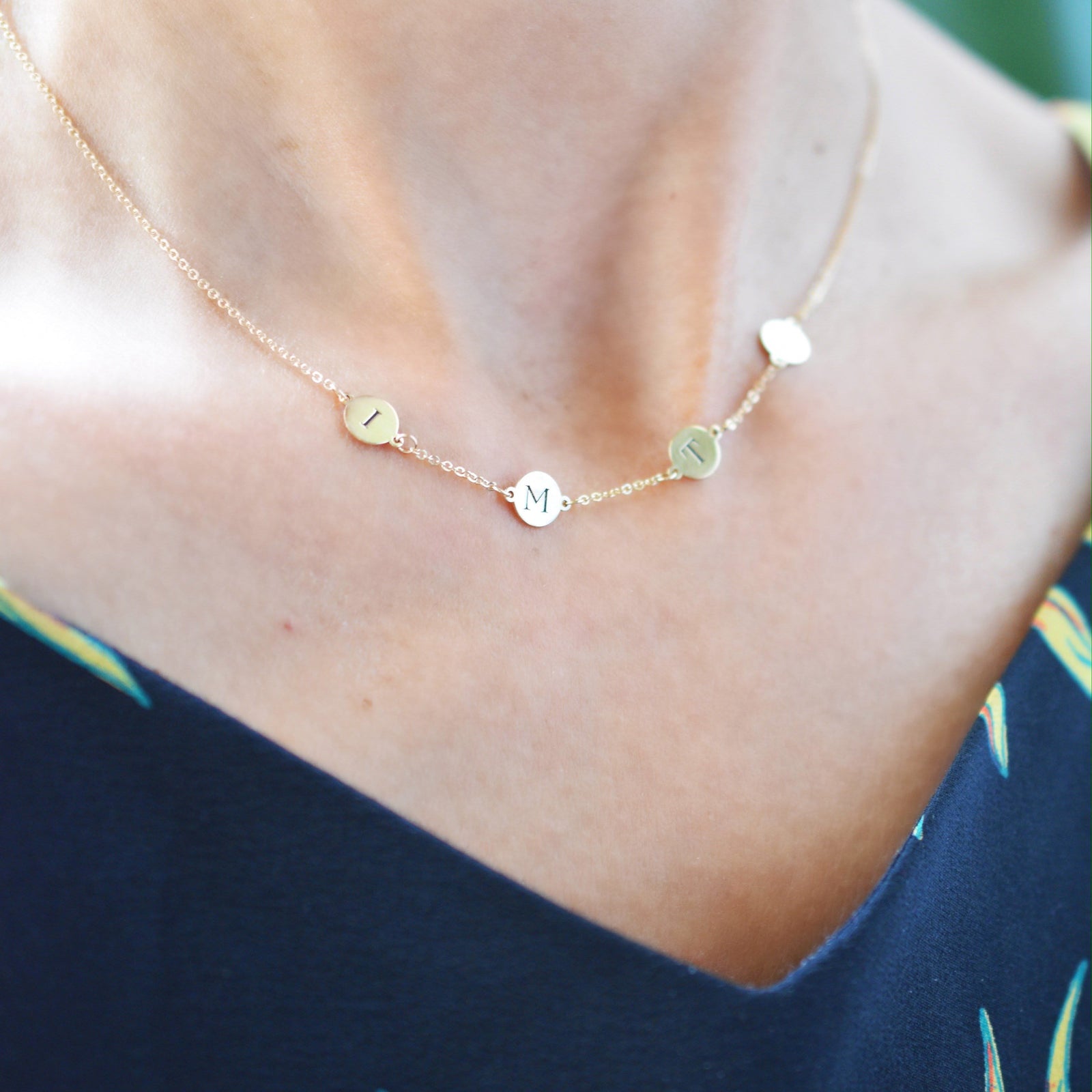 Woman wearing a 14k yellow gold cable chain necklace featuring four 1/4” flat discs engraved with letters