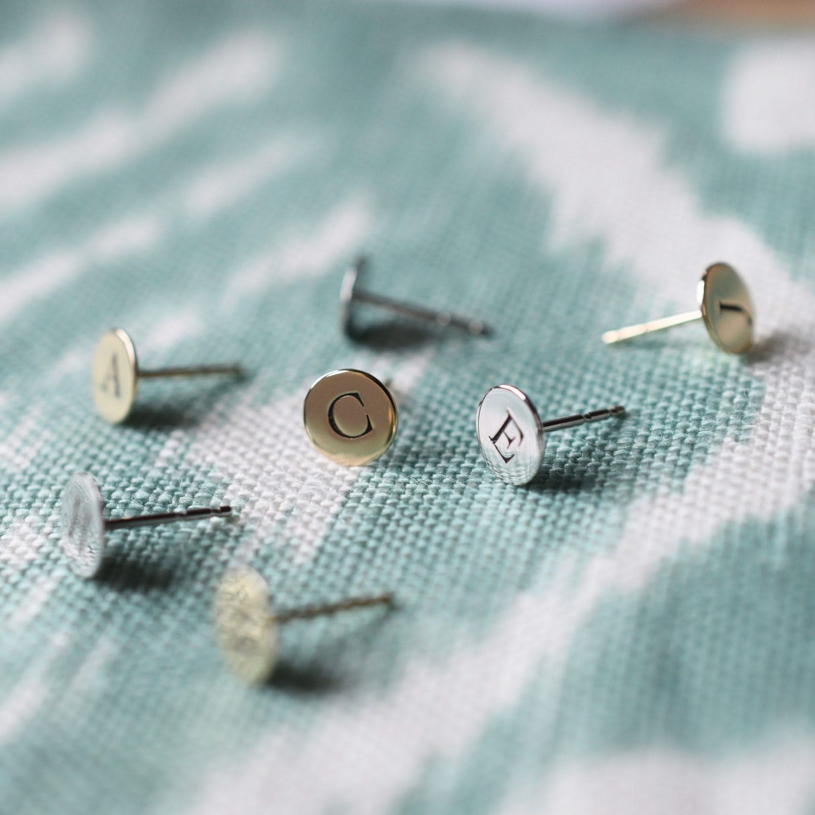 Several 14k yellow gold stud earrings each featuring one 1/4” letter-engraved flat disc