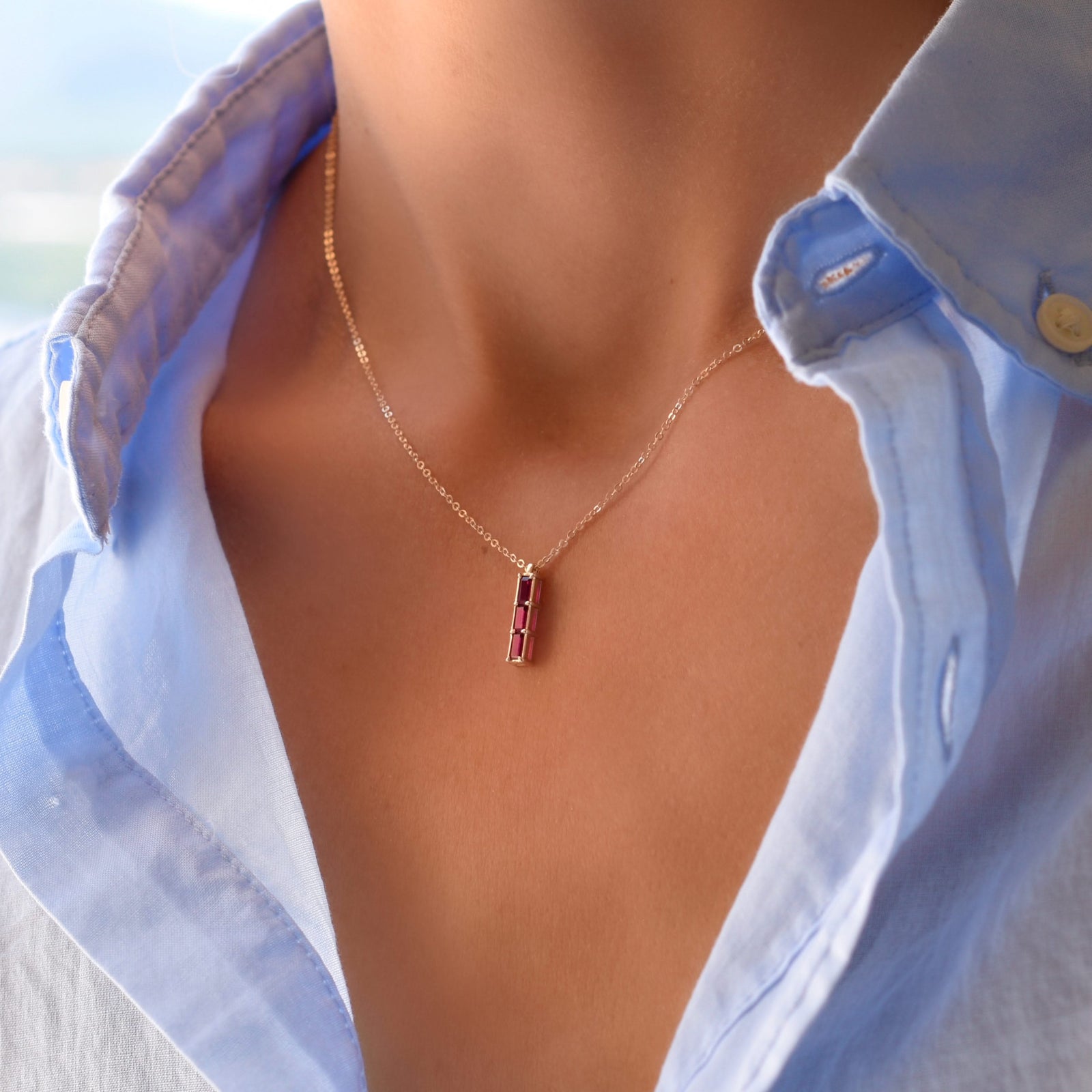 Woman wearing a Providence Ruby vertical bar pendant featuring 3 petite baguette stones set in 14k yellow gold