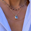 Woman wearing 3 Haverhill necklaces and a blue and white pinstripe v neck shirt. Top is Newport saphhire necklace with bezel set stones, next is Blue Topaz pendant with large emerald cut stone, bottom is Mia rolo chain in yellow gold