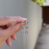 Fingers holding a pair of Newport Grand 3 Aquamarine earrings, each featuring 6mm briolette cut, bezel set gemstones.