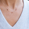Woman wearing a Bayberry 3 Ruby necklace featuring three 4mm briolette cut, bezel set gemstones on a 1.17mm cable chain.