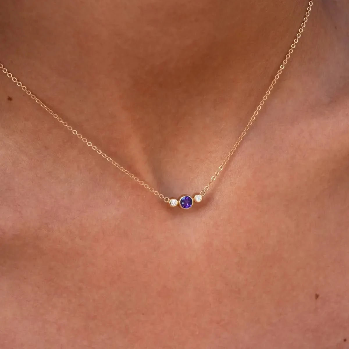 Close-up of Barrington 3 Stone Necklace showcasing bezel set Amethyst center stone with Diamond side stones in 14k yellow gold.