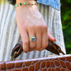 Close-up of a woman's hand holding a suitcase and wearing a Rosecliff Stackable ring, Warren ring, and two Newport bracelets.