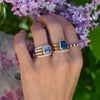 Close-up of a woman's hand wearing stacked Rosecliff and Warren rings featuring sapphire, Nantucket blue topaz, and diamonds.