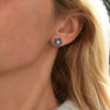 A woman wearing a 14k yellow gold Greenwich Flower earring featuring five 4mm alexandrites and one 2.7mm diamond.