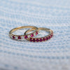Two Haverhill Rosecliff Rings on a blue and white fabric background. One ring has eleven 2 mm rubies, one has rubies and diamonds.