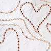 Necklaces and bracelets scattered on a white marble background with two necklaces forming a heart shape. 