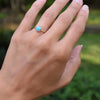 A woman's hand wearing a Grand Turquoise ring featuring a 6mm briolette cut, bezel set gemstone on a 1.6mm band.