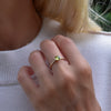 Woman's finger wearing a Grand Peridot ring featuring a 6mm briolette cut, bezel set gemstone on a 1.6mm band.