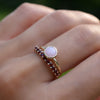 Woman's finger wearing two stacked rings including a Rosecliff Garnet Stackable ring and Grand Pink Opal ring.