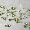 Scattered assortment of peridot gemstones in various cuts and sizes on a white fabric background.