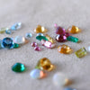 Various assortment of differently shaped and colored gemstones on a white velvet background.