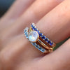 Close-up of a hand wearing two 14k yellow gold stacked Rosecliff rings with a Grand Moonstone ring in between.