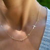 Woman wearing a personalized Classic Cross & 4 Birthstone necklace featuring one 0.5in cross and 4mm bezel set gemstones.