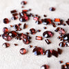 Scattered assortment of loose garnet gemstones of various cuts and sizes on a white fabric background.