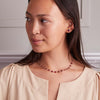 Woman wearing matching 14k yellow gold Grand necklace and a pair of Grand stud earrings featuring one 6 mm briolette cut Ruby