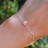 Woman wearing a Grand 1 Birthstone bracelet featuring one 6mm bezel set pink opal gemstone on a 1.17mm cable chain.