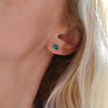 Woman wearing a 14k yellow gold Grand stud earring featuring one 6 mm briolette cut bezel set emerald on her ear.