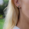 Woman wearing a 14k yellow gold Grand stud earring featuring one 6 mm briolette cut bezel set emerald