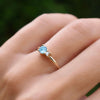 Hand wearing a Greenwich ring featuring one 4 mm round cut Nantucket blue topaz and one 2.1 mm diamond prong set in 14k gold