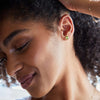 Woman adorned with 14k yellow gold Grand stud earrings each featuring one 6 mm briolette cut peridot