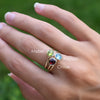 Woman's hand wearing three stacked Grand rings featuring 6mm peridot, Nantucket blue topaz, and garnet in 14k yellow gold.