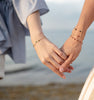 A close-up of two friends holding hands while each wearing layered personalized classic, Newport, and letter disc bracelets.