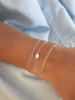 Wrist wearing a Classic 1 White Topaz bracelet, Letter H bracelet, and Bayberry 3 Peridot bracelet, all in 14k white gold.